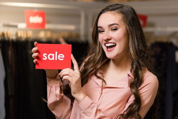 Молодая женщина держит красные вывески со словом продажи