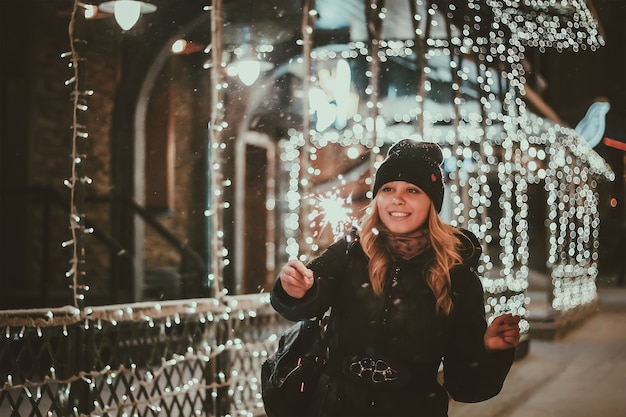 A young woman holds a sparkler in her hands on the background of blue blurred bokeh lights