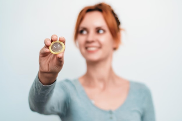 The young woman holds an unpacked condom in her hand The concept of safe sex