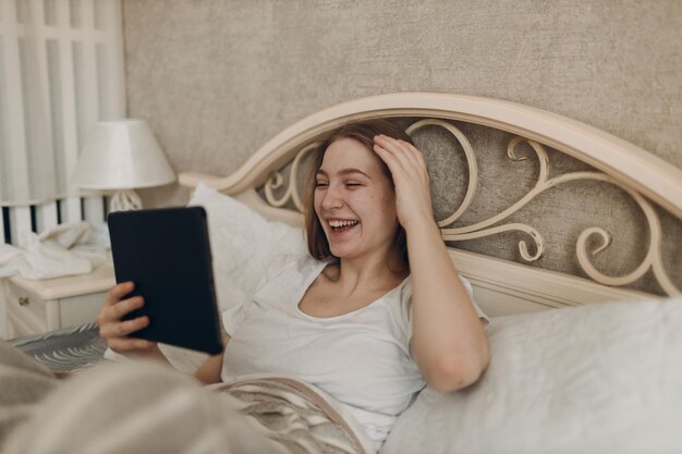 Young woman at home indoor lying on bed in bedroom with digital tablet