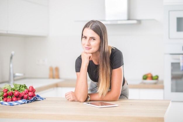 Giovane donna in cucina di casa con tablet.