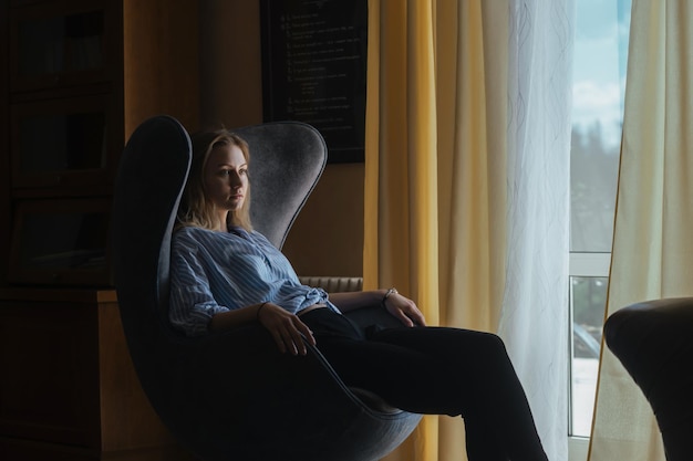 a young woman at home sits in a large armchair and rests in the twilight of the room