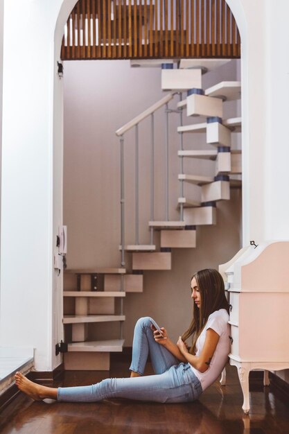 Young woman at home sitting on the floor using cell phone