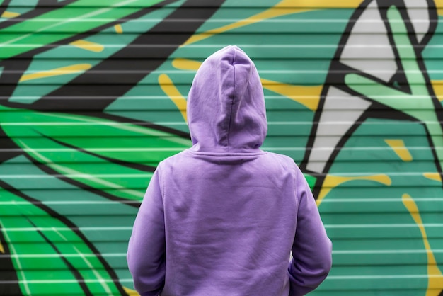 Young woman in hood in purple violet hoodie from back on green modern background copy space mockup