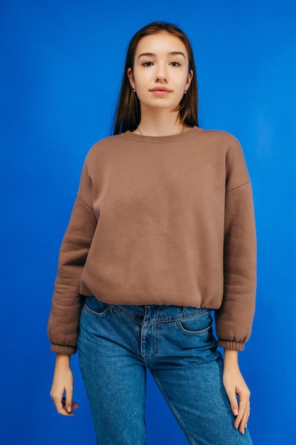 Young woman in hoodie posing in studio on blue background