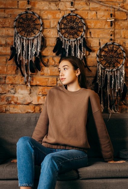 Young woman in hoodie posing in studio on brick wall space