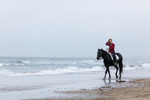 Молодая женщина на лошади на пляже