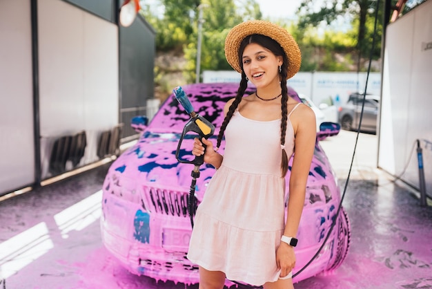 Young woman hose stands in front of a car covered in pink foam