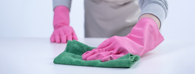 Young woman housekeeper in apron is cleaning wiping down table surface with wet rag spraying bottle cleaner to prevent disease spreading