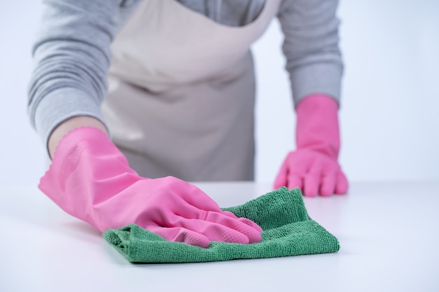 young woman housekeeper in apron is wearing pink gloves to clean the table, concept of preventing virus infection, housekeeping service, close up.