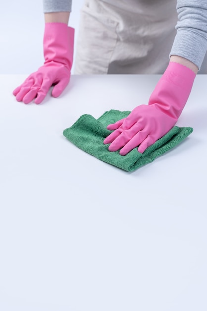 Young woman housekeeper in apron is wearing pink gloves to clean the table, concept of preventing virus infection, housekeeping service, close up.