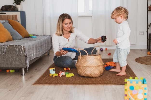 若い女性の主婦は自宅で幼い息子と一緒におもちゃをバスケットに入れる