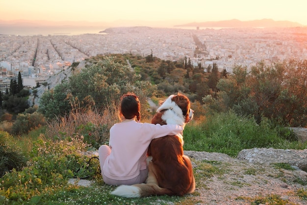 写真 若い女性が野原に座っているとき犬を抱きしめますアテネギリシャ日没からの本当の暖かい光