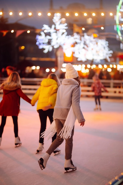 夕方のお祝いのクリスマスフェアでスケートリンクで若い女性のアイススケート。周りのライト。