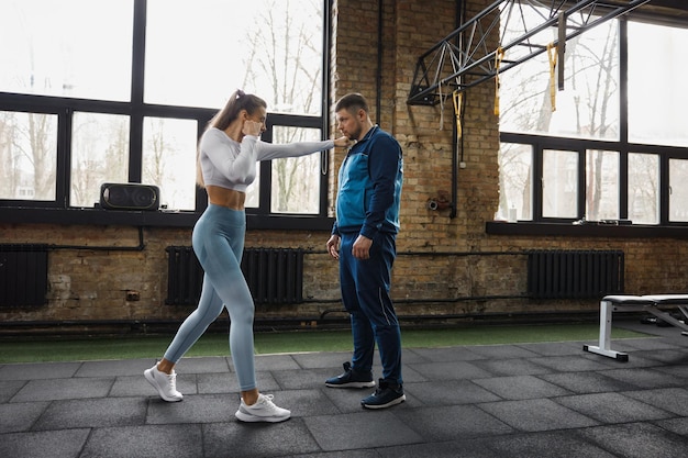 Young woman improving fighting skills with personal instructor at gym