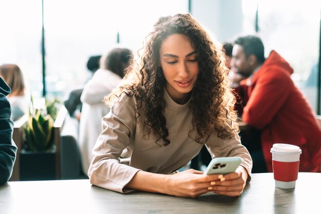 写真 カフェで携帯電話からメッセージを読んでいる若い女性