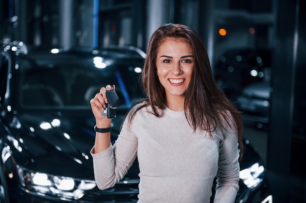 Фото Молодая женщина в повседневной одежде, стоя возле современной черной машины с ключами в руках.