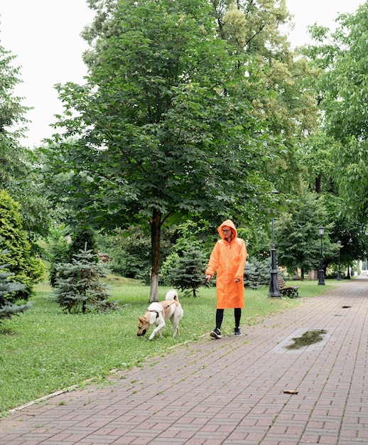 Фото Молодая женщина в оранжевом плаще гуляет со своей собакой в парке