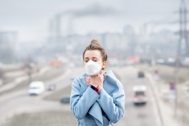 Фото Молодая женщина в защитной маске плохо себя чувствует в городе с загрязнением воздуха от движения и производства. концепция смога