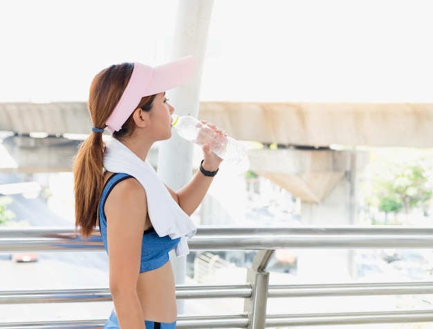 写真 橋の上に立って水を飲むスポーツ服を着た若い女性