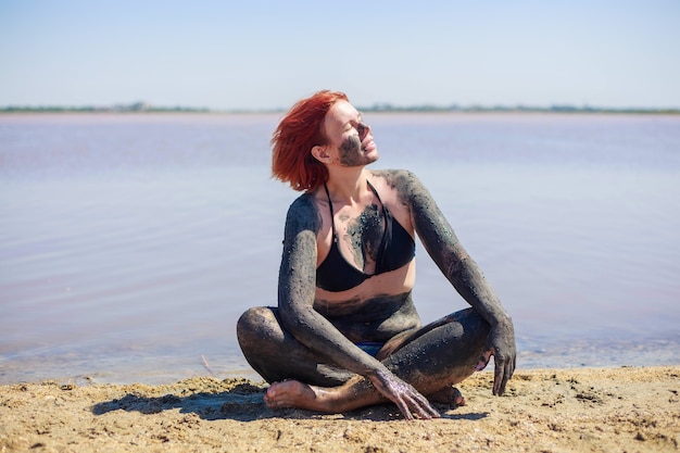 水着姿の若い女性は、塩漬けの湖から供給された顔と体に天然ミネラル泥を取っています