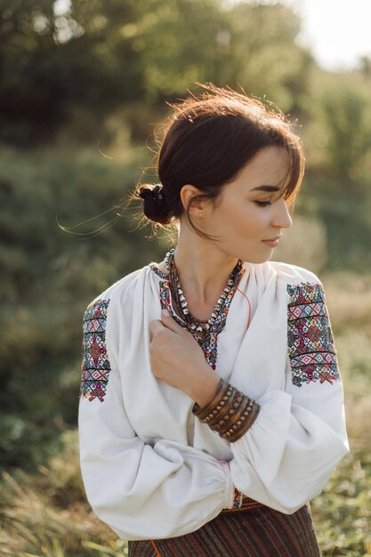 Фото Молодая женщина в традиционной национальной вышитой рубашке и юбке на природе на закате этническая национальная одежда в стиле вышитой рубашки