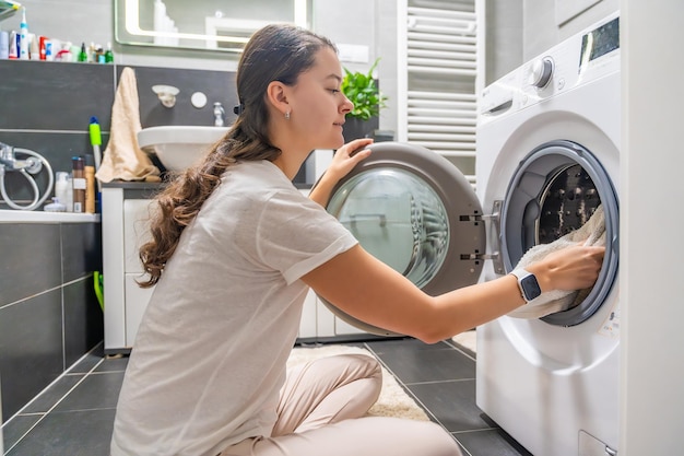 young woman inserting clothes inside the washing machine in home bathroom