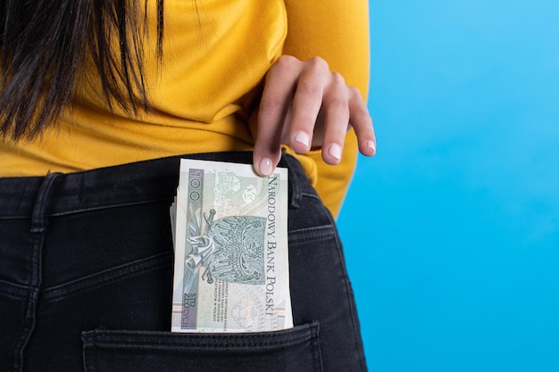 A young woman inserts a bundle of paper banknotes into the back pocket of jeans