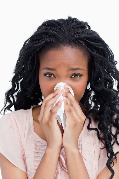 A young woman is blowing her nose in a tissue