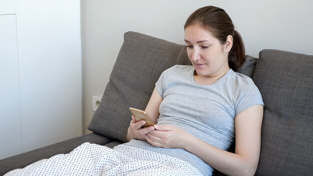若い女性が居間のソファに座ってスマートフォンを閲覧しています。彼女は面白いものを見て笑っています。