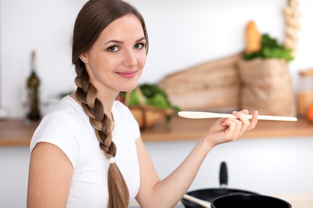 Молодая женщина готовит на кухне Домохозяйка пробует суп деревянной ложкой