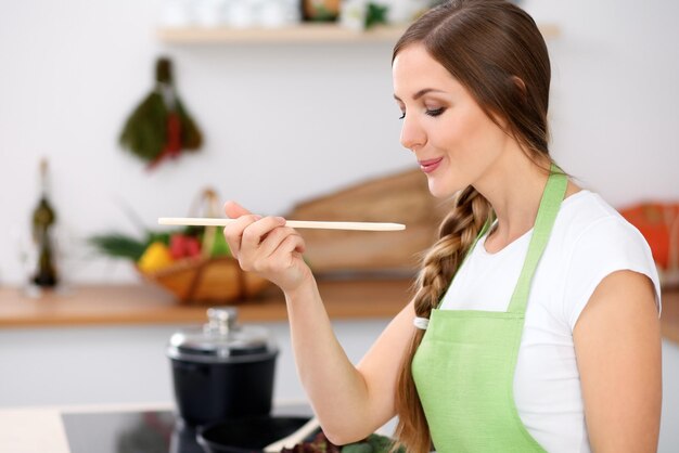 젊은 여성이 부엌에서 요리를 하고 있다 주부가 나무 숟가락으로 수프를 맛보고 있다