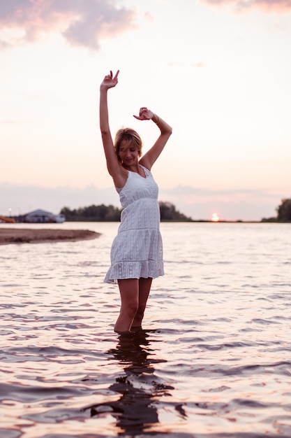 Una giovane donna sta ballando nell'acqua foto di una bella bionda felice in un abito estivo bianco e argu...