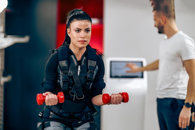 Young woman is doing EMS personal training with coach in the gym.