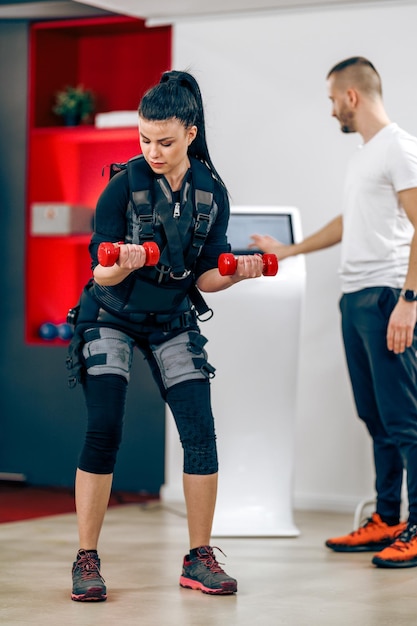 Foto la giovane donna sta facendo l'allenamento personale ems con l'allenatore in palestra.