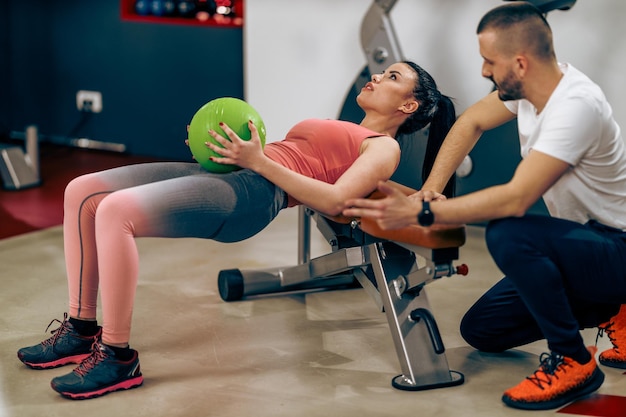 La giovane donna sta facendo l'allenamento per gli addominali con il personal trainer in una palestra.