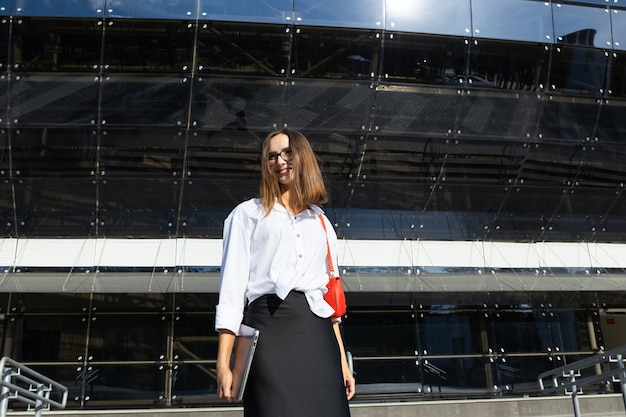 A young woman is dressed in business style holds a laptop in her hands on the street