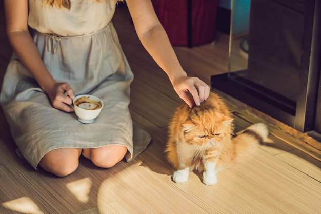 Young woman is drinking coffee and stroking the cat.