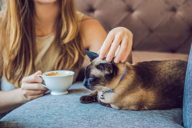 Young woman is drinking coffee and stroking the cat.