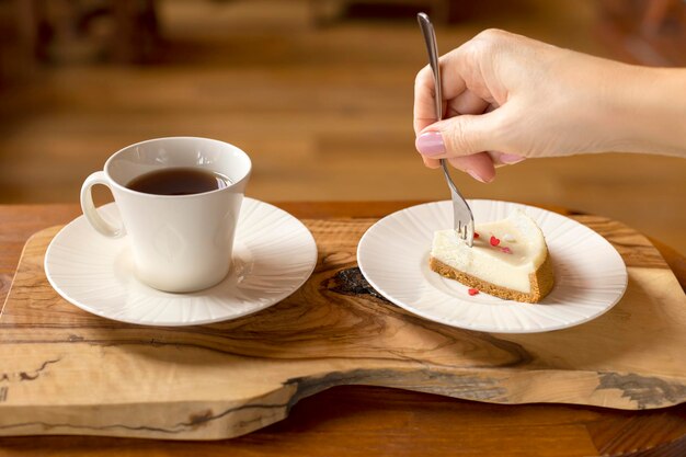 A young woman is eating cheesecake and drinking tea a closeup of a female hand using a fork to take a piece of cake