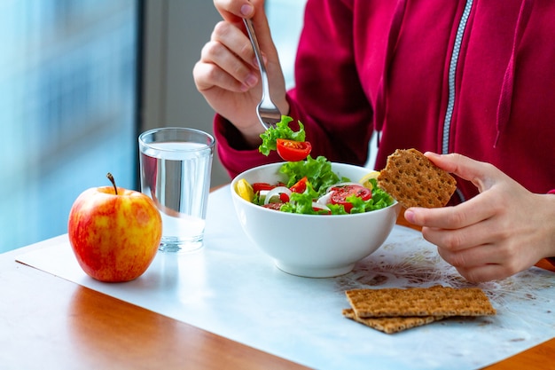 若い女性は、さわやかなライ麦パンと健康的で新鮮な野菜サラダを食べています。ダイエットと健康的なライフスタイルのコンセプト。ダイエット食品。適切な栄養と正しい食事