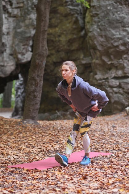 Young woman is engaged in fitness in the autumn park among the rocks The girl goes sports in nature