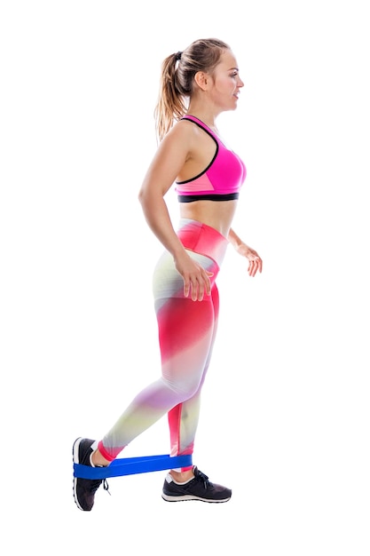 A young woman is engaged in fitness with an elastic band on her legs Beautiful brownhaired woman in bright sportswear Health sports and activity