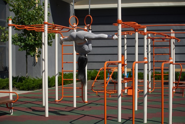 The young woman is engaged on gymnastic rings. She hangs upside down, legs in twine.