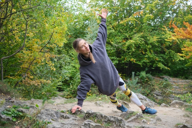 写真 若い女性は岩の間の秋の公園でフィットネスに従事しています女の子は自然の中でスポーツに行きます