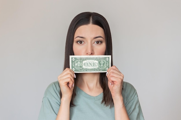 Photo young woman is holding dollar bill in her hands and covering her mouth with it financial dependence