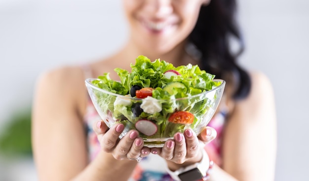 A young woman is holding a healthy spring salad in a glass bowl