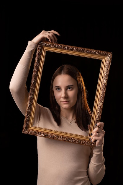 A young woman is holding a picture frame Black background Psychological portrait introspection reflection concept