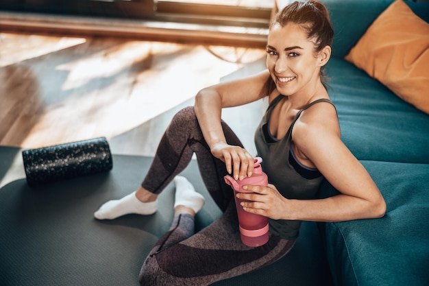 Young woman is holding water bottle and preparing for training at home.