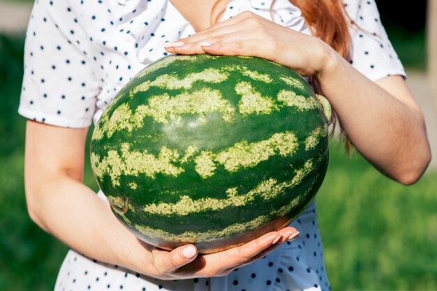 A young woman is holding a whole watermelon.